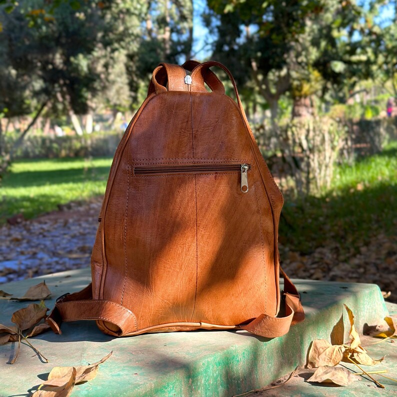 the back side of a womens backpack, rucksack, and zipped pocket. zipped straps