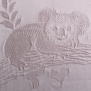 Puede incluir: Una manta de punto de color lila claro con un diseño de koala. El koala está sentado en una rama con un corazón debajo. La manta tiene un aspecto texturizado y es adecuada para un bebé o un niño.