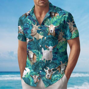 Könnte beinhalten: Kurzärmeliges Hemd mit einem Muster aus Ziegen und tropischen Blättern in Grün und Blau. Das Hemd hat einen klassischen Kragen und einen Knopfverschluss. Die Ziegen sind in verschiedenen Posen und Farben.