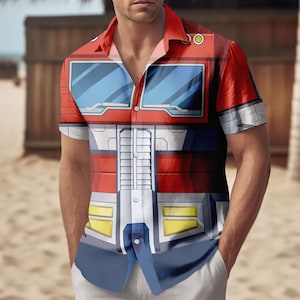 May include: Red, white, blue, and yellow short-sleeve button-down shirt featuring a graphic design. The shirt's design resembles a robot's chest and head. The shirt has a classic collar and is worn by a person.