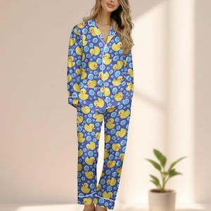 Puede incluir: Conjunto de pijama azul con un estampado de patitos de goma amarillos y burbujas azules. La parte superior de manga larga y los pantalones tienen ribetes blancos. El pijama está hecho de un material suave y cómodo.