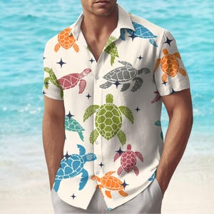 Puede incluir: Camisa de manga corta color crema con un estampado de tortugas de colores. Las tortugas son en tonos naranja, verde, azul, gris y rojo, con detalles de estrellas azules oscuras. La camisa la lleva una persona en una playa.