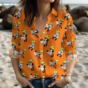 May include: Orange button-down shirt with a repeating pattern of the cartoon character Goofy. The long-sleeved shirt has a classic collar and button closure. The Goofy character is depicted in black, white, and green.