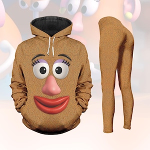 May include: A brown hoodie and leggings set featuring a cartoon face design. The hoodie has a black hood lining, white drawstrings, and a large face graphic with big eyes, a pink nose, and red lips. The leggings are brown.