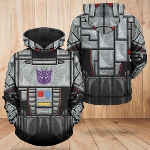 May include: A long-sleeved hooded sweatshirt featuring a grey and black mechanical armour pattern. The front displays a purple Decepticon logo, a red square, a blue circle, and a yellow rectangle. The design includes a hood and ribbed cuffs.