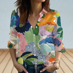 以下が含まれることがあります： 青、ピンク、黄色、緑の色合いの鮮やかな花柄のボタンダウンシャツ。長袖シャツはVネックで、軽量の生地で作られています。青いジーンズと合わせています。