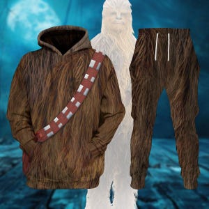 May include: Brown hoodie and matching pants set with a Chewbacca design. The hoodie features a hood, front pocket, and a red and white bandolier. The pants have a drawstring waist. The set is designed to resemble the Star Wars character.