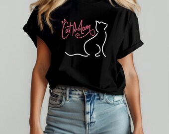 May include: Black t-shirt featuring a white cat outline and the pink text "Cat Mom". The design includes a stylized cat face above the word "Mom". The shirt is a classic crew neck style.