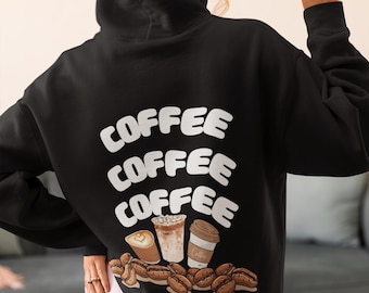 May include: Black hoodie with the word "COFFEE" repeated three times in white, along with illustrations of coffee drinks and beans. The person is wearing the hoodie and giving a peace sign.