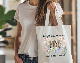 May include: Cream-colored tote bag with the text "Fully Booked Weekend" and "Zero Shelf Control". The bag features a floral design with books in the center. The person is wearing a white t-shirt and blue jeans.