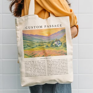 Könnte beinhalten: Cremefarbene Tragetasche mit Landschaftsmalerei und dem Text "CUSTOM PASSAGE". Das Gemälde zeigt einen Sonnenuntergang über einem Tal mit einem Haus. Die Tasche hat ein rechteckiges Design und einen langen Griff.