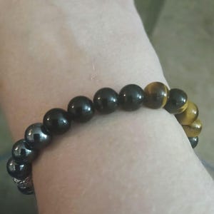 May include: A beaded bracelet featuring a mix of black and tiger's eye beads. The bracelet is strung on a stretchy cord and is worn on a wrist. The beads are round and have a polished finish.