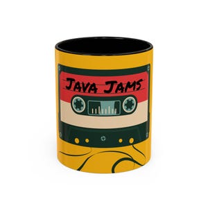Puede incluir: Una taza de café amarilla con interior negro. La taza presenta un diseño de cinta de cassette retro con las palabras "JAVA JAMS" en rojo. El diseño de la cinta de cassette incluye elementos rojos, beige y verdes.