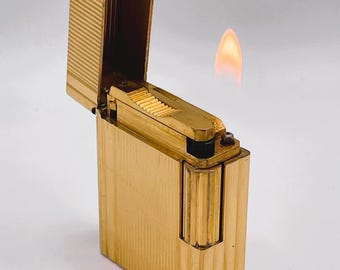 Könnte beinhalten: Ein goldfarbener Feuerzeug mit geripptem Design und einer Flamme, die aus der Oberseite kommt.