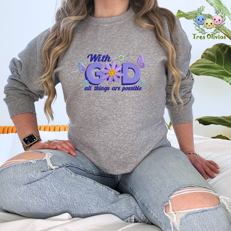 Pu&ograve; includere: Una felpa grigia con il testo "With God all things are possible" in lettere viola con accenti floreali.