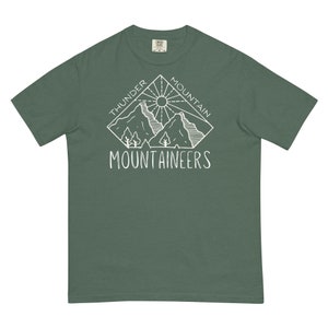 May include: A green t-shirt with a white graphic design of a mountain range with a sun and the text "Thunder Mountain Mountaineers".