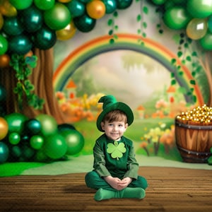 May include: A child in a green leprechaun costume sits on a wooden floor. The backdrop features balloons, a rainbow, and a pot of gold. The costume includes a hat and a shamrock.