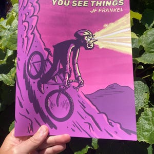 May include: A book cover with a vibrant magenta and purple background featuring a black ink illustration of a cyclist riding down a steep hill. The text at the top reads OUT RIDING BIKES YOU SEE THINGS and JF FRANKEL. The cyclist has light beams emitting from their eyes.