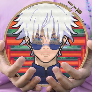 May include: Cross-stitch embroidery hoop featuring a pixelated anime character with white hair, blue eyes, and a blue shirt. The background is a colorful pixelated pattern.