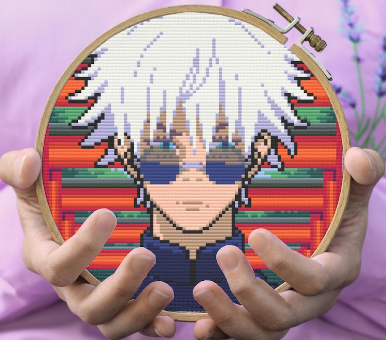 May include: Cross-stitch embroidery hoop featuring a pixelated anime character with white hair, blue eyes, and a blue shirt. The background is a colorful pixelated pattern.