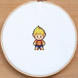 May include: Cross-stitch embroidery of a pixelated character with blonde hair, a red and yellow striped shirt, blue shorts, and red shoes.