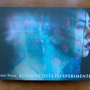 May include: A book cover with a blue and purple floral pattern. The title of the book is "Authentizitätsexperimente" and the author is Renée Nesca.