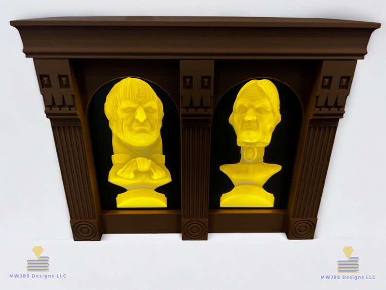 May include: A brown wooden frame with two yellow illuminated busts of people inside. The frame is mounted on a white wall.