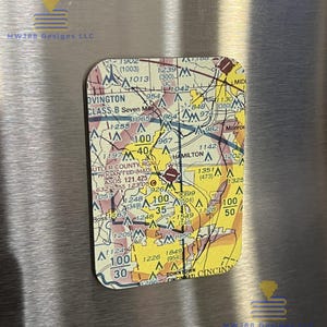 May include: Rectangular magnet featuring a detailed aviation sectional chart of the Cincinnati area. The magnet has rounded corners and includes text such as "OVINGTON" and "DOWNTOWN CINCINNATI". The magnet is affixed to a metallic surface.