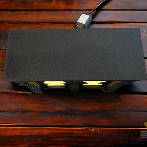 May include: A black and white 3D printed model of a building with a black roof and yellow windows. The model is lit from the inside, casting a warm glow.