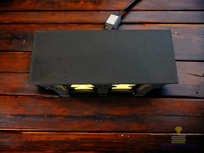 May include: A black and white 3D printed model of a building with a black roof and yellow windows. The model is lit from the inside, casting a warm glow.