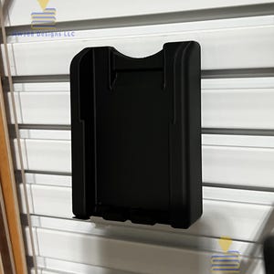 Peut inclure: Un support de téléphone en plastique noir avec une fente pour un téléphone. Le support est monté sur un mur blanc.