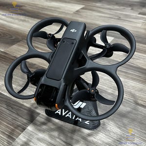 Puede incluir: Dron negro con cuatro hélices y un soporte negro. El dron tiene un diseño elegante con detalles en naranja y el texto "AVATA Z" en el soporte. Diseñado para fotografía y videografía aérea.