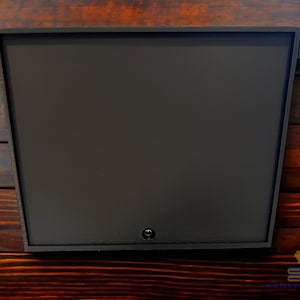 May include: A dark brown, rectangular mailbox with a single keyhole on the front. The mailbox is mounted on a wooden wall.