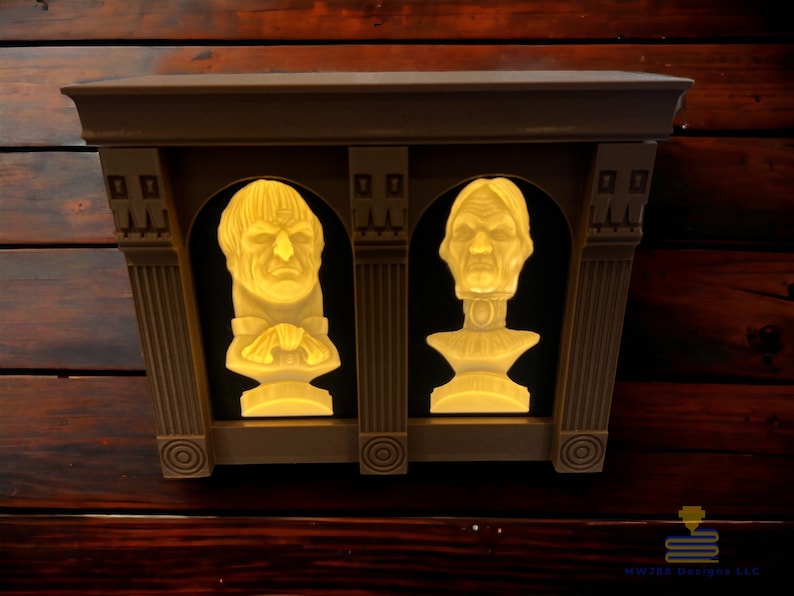 May include: A wall-mounted decorative shelf with two illuminated busts of people. The shelf is made of brown wood and has a white trim. The busts are made of white plaster and have a realistic appearance.