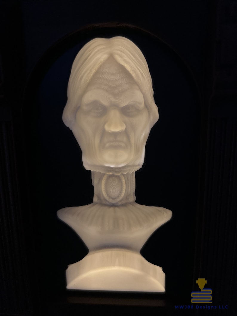 May include: A white bust sculpture of a woman with a stern expression. The sculpture is detailed with a textured surface and a decorative collar.
