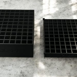 Könnte beinhalten: Zwei schwarze, quadratische Organizer mit einem Rastermuster. Der größere Organizer ist ein Würfel, während der kleinere ein flaches Tablett ist. Beide haben eine Reihe kleiner quadratischer Fächer. Der Text "MW3RS Designs LLC" ist sichtbar.