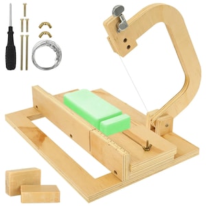May include: A wooden soap cutter with a wire blade, a guide fence, and a tensioning knob. Includes a screwdriver, metal screws, wing nuts, and a coil of wire. Two light green soap bars are on the cutting platform, with two tan bars nearby.