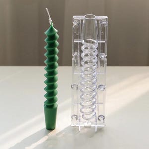 May include: A green spiral candle with a white wick stands next to a clear plastic candle mould. The candle has a textured, ridged design. The mould is rectangular and has a spiral cavity to match the candle's shape. Candle making supplies.