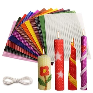 May include: A selection of colourful beeswax sheets and lit candles. The candles feature various designs, including a floral pattern, stars, and a spiral. A bundle of white wick is also present.