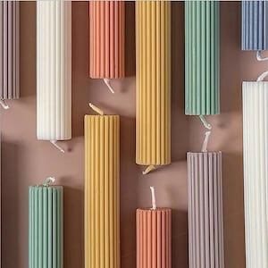 Peut inclure: Assortiment de bougies piliers colorées avec une texture côtelée. Les bougies sont disposées en rangée sur une surface brune.