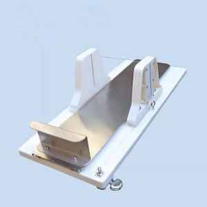 May include: White plastic food slicer with a stainless steel blade and a clear plastic guard. The slicer has a white base and a white handle.