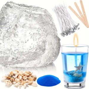 Könnte beinhalten: Ein Kerzenherstellungsset mit einem großen Block aus klarem Gelwachs, einem Bündel weißer Dochte mit Metallfüßen, drei hölzernen Zentrierstäben, einer Ansammlung kleiner Muscheln, blauem Sand und einer brennenden Kerze mit Seestern.