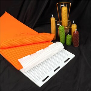 May include: Two silicone honeycomb candle moulds, one orange and one white, with several finished beeswax candles in various colours.