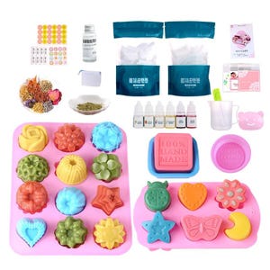 May include: A soap-making kit with various components. Includes silicone molds in pink, with flower, star, and heart shapes. There are also bottles of liquid, a measuring cup, and a pink bear-shaped mold. The kit also contains a soap base and other ingredients.