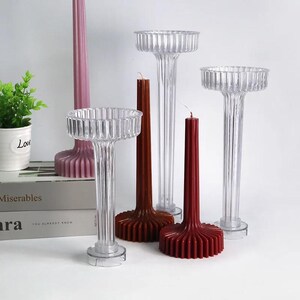 May include: Three clear plastic candle holders with fluted columns and a wide, round base. The holders are empty, but there are three red candles in the image, two of which are in the holders.