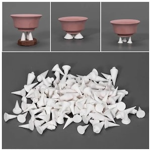 May include: Dusty rose-coloured ceramic tea cups, each with white, cone-shaped feet. The image also shows a pile of individual white feet, possibly replacement parts or accessories for the cups.