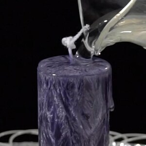May include: A purple candle with a white wick is being poured with clear wax. The candle has a textured surface.