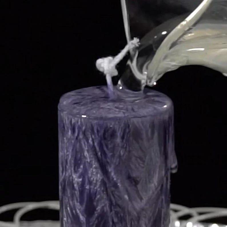 May include: A purple candle with a white wick is being poured with clear wax. The candle has a textured surface.