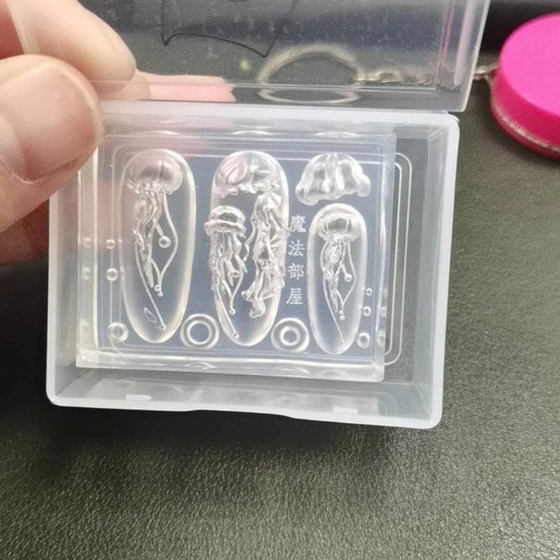 Puede incluir: Moldes de silicona transparente para decoraci&oacute;n de u&ntilde;as con dise&ntilde;os de medusas. Los moldes est&aacute;n en una caja de pl&aacute;stico transparente, con dise&ntilde;os de medusas de varios tama&ntilde;os y formas. El texto "魔法部屋" es visible en el molde.