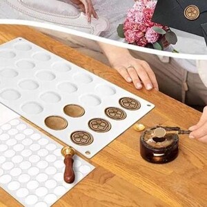 Op de afbeelding: Een witte siliconen mal met 28 ronde holtes voor het maken van waszegels. Een houten handvat met een metalen punt wordt gebruikt om was te smelten en op de zegels aan te brengen. Een vel wit papier met 50 ronde stickers is ook inbegrepen.